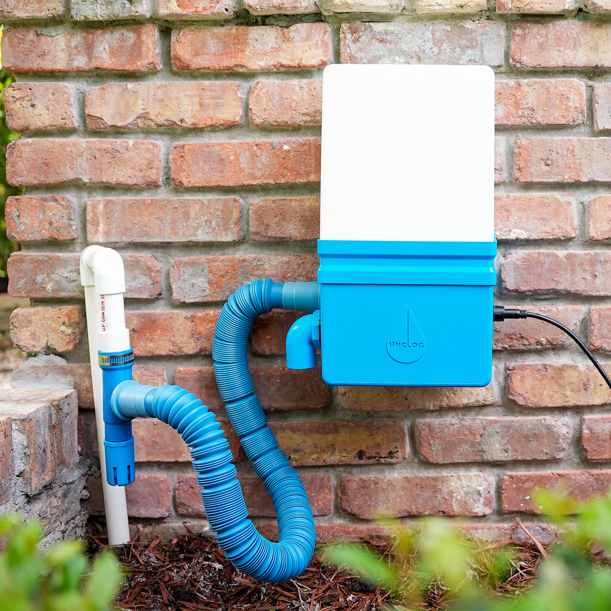 Production Unclog unit mounted on a brick wall and connected to an outdoor condensate drain through its blue hose