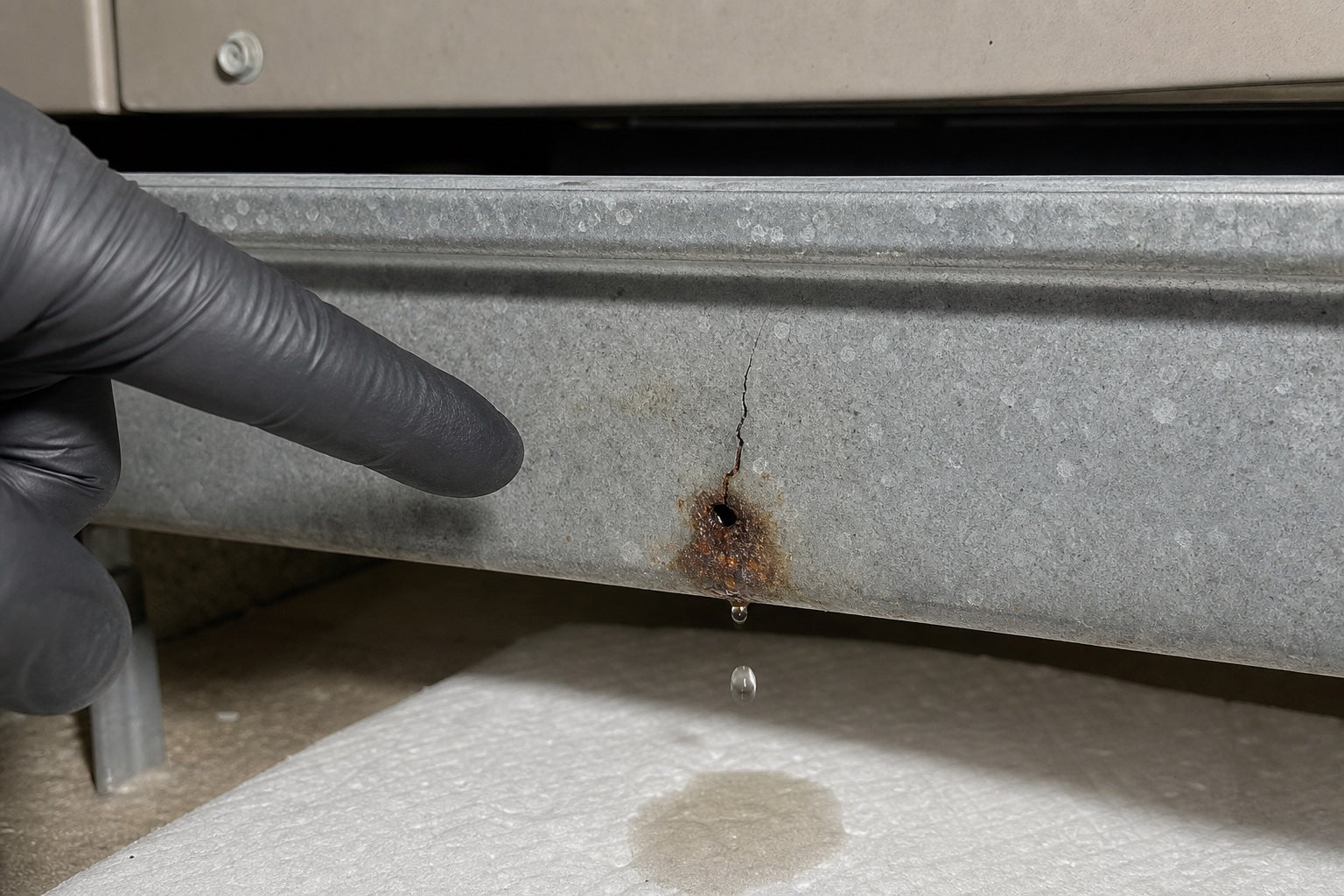 Hairline crack and localized rust-through leaking from an A/C drain pan