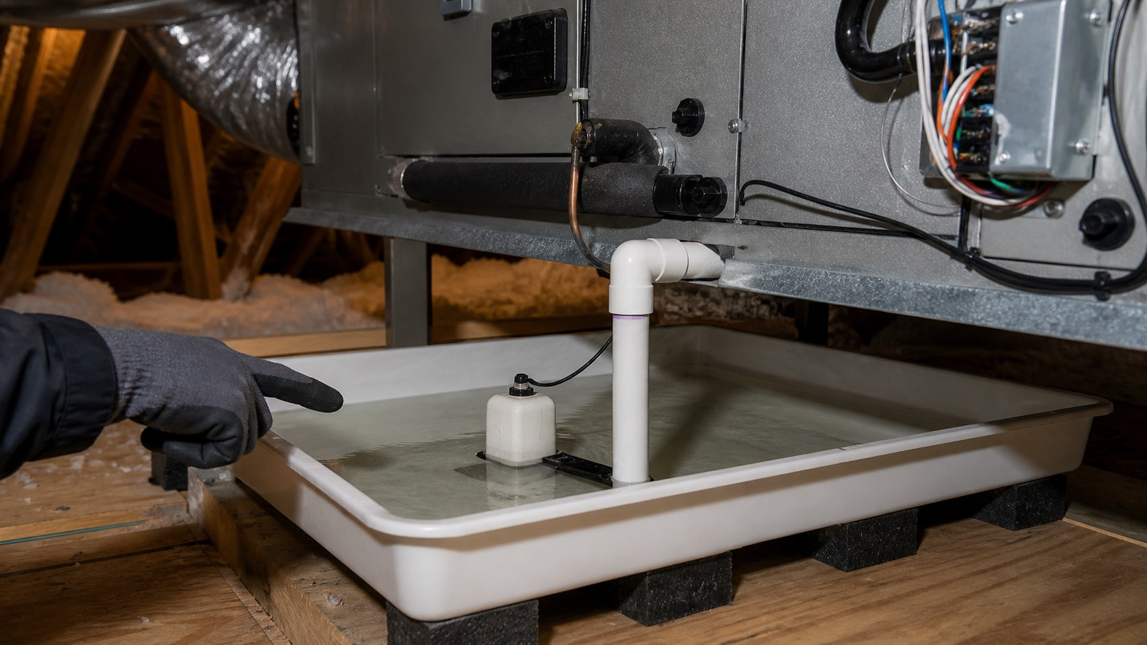 Technician safely inspecting shallow water and a raised float switch in an auxiliary A/C drain pan