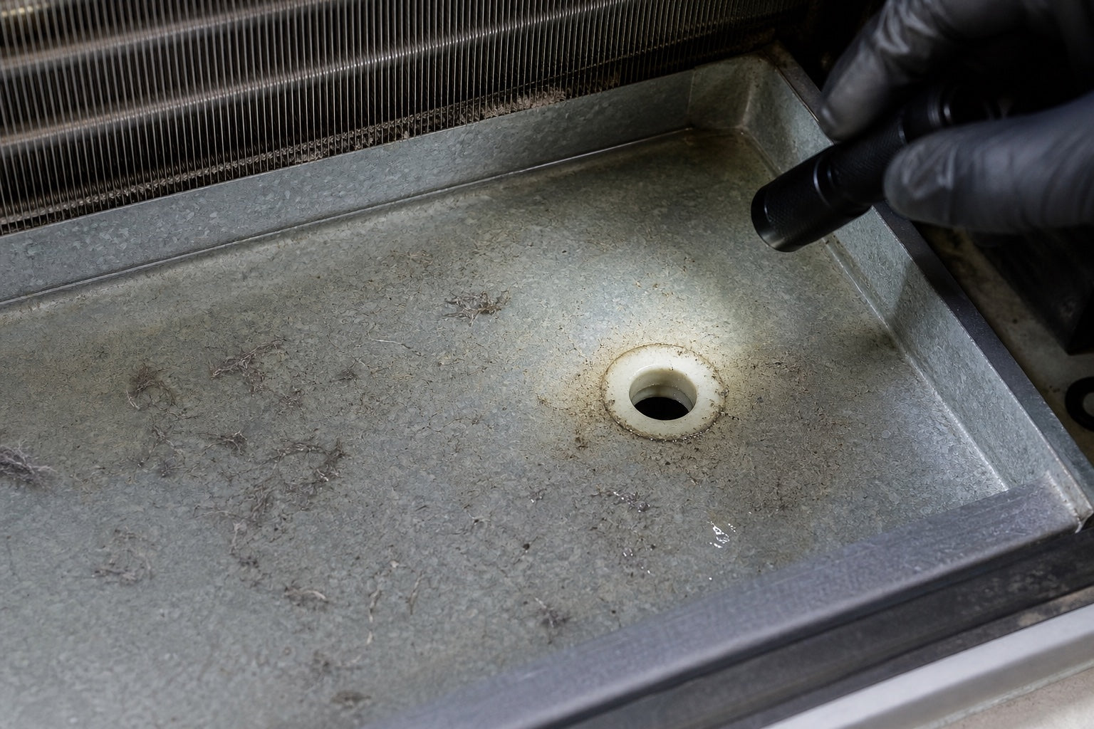 Technician inspecting a thin layer of dust and residue near an A/C condensate pan outlet